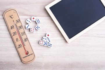 A thermometer and two group of dices arrange in different formations with blackboard on top of wooden table. Education, health and entertainment conceptual.