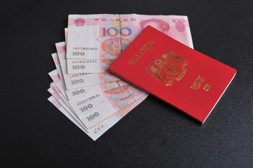 Malaysian passport with Chinese yuan on top of black backround. Travel and vacation conceptual.