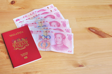 Malaysian passport with Chinese yuan notes on top of a wallet on a wooden table. Travel and vacation conceptual.