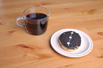A donut with peanut as a topping and a cup of coffee on top of wooden table.