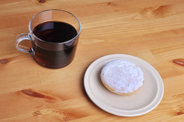 A donut with peanut as a topping and a cup of coffee on top of wooden table.
