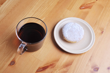 A donut with peanut as a topping and a cup of coffee on top of wooden table.