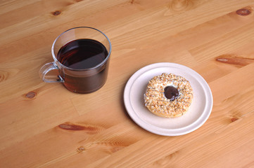 A donut with peanut as a topping and a cup of coffee on top of wooden table.