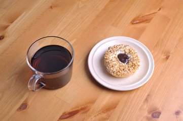 A donut with peanut as a topping and a cup of coffee on top of wooden table.