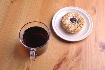 A donut with peanut as a topping and a cup of coffee on top of wooden table.