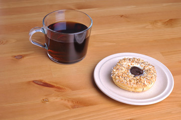 A donut with peanut as a topping  and a glass of coffee on top of wooden table.