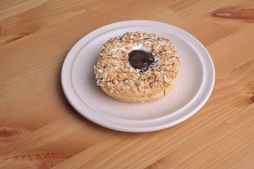 A donut with peanut as a topping on top of wooden table.