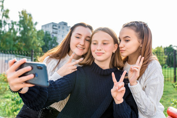 3 girls girlfriends teenagers 14-15 years old, selfie photo phone, autumn park, relaxing after classes college school, watching videos social networks smartphone screen. In casual wear, sweater jeans.