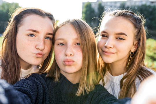 3 girls girlfriends teenagers, 14-15 years old, taking selfie photo on telephone camera, on autumn day in city on street, resting after classes college and school. In everyday clothes, sweater.