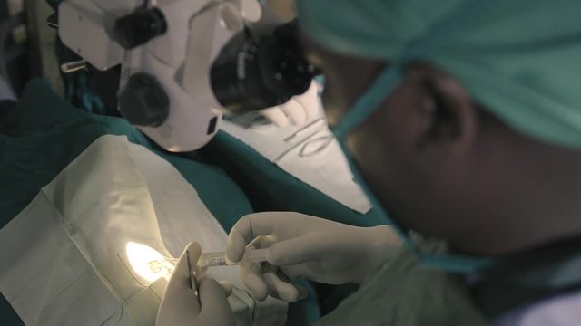 close up of doctor using tweezers in eye and after taking a syringe to insert fluids into the eye during surgery in Africa