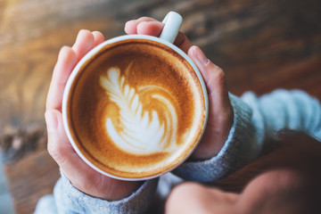 Top view image of a woman holding a cup of hot latte coffee on wooden table