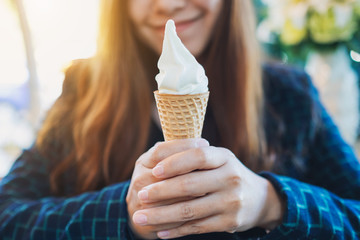 Closeup image of a woman holding and eating soft serve ice cream waffle cone