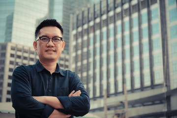 Confident male business executive  with arms crossed standing in front of office building