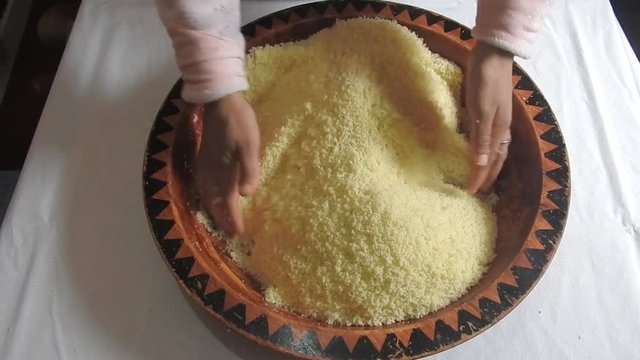 Woman rolling hot semolina of couscous between  her fingers in a wooden dish at home  after steaming it .Close Up 
of plate Couscous. Top view .Morocco