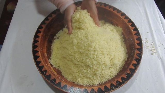 Woman rolling hot semolina of couscous between  her fingers in a wooden dish at home  after steaming it .Close Up 
of plate Couscous. Top view .Morocco