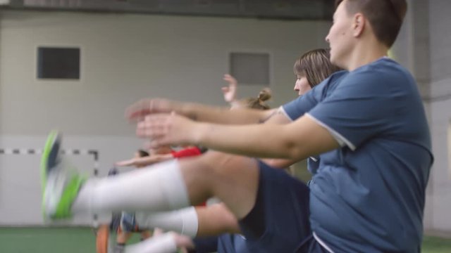 Side view shot of young professional female athletes performing walking front leg raises while training together on indoor soccer field