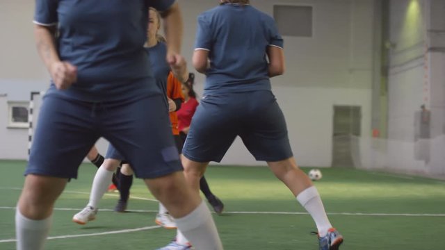 Side view tracking shot of professional team of young female athletes in soccer uniform doing sidestep warmup exercise while practicing on indoor sports field