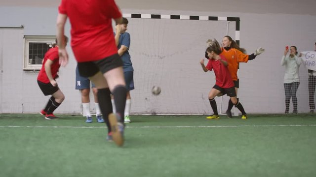 Female soccer player shooting free kick, scoring a goal and then huddling and jumping with team while celebrating victory during match on indoor sports field