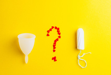 Fototapeta premium Menstrual cup, tampon and question from red hearts on yellow background. Alternative feminine hygiene product during the period. Women health concept. Flat lay. Copy space.