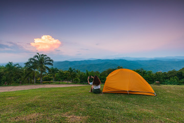 A girl traveler with her tent on the cliff in the evening.