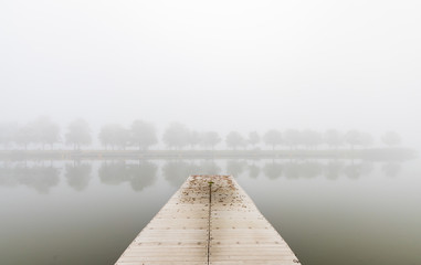 Floating fishing pier in the fog with treeline in background © Martina
