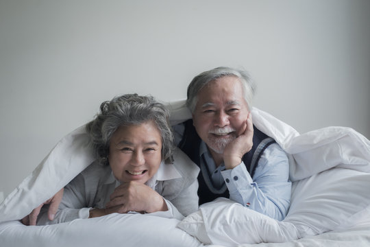 elderly couple caucasian senior man and woman sleep on bed and smiling in white blanket in bedroom, retirement health care with love lifestyle concept