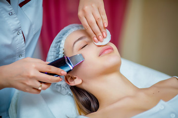 Woman receiving ultrasonic facial exfoliation at cosmetology salon. Procedure clearing clogged...