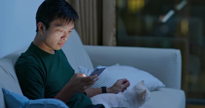 Man cuddle on his Pomeranian dog at home with using cellphone