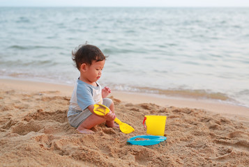 Little asian baby boy playing sand at beach alone.