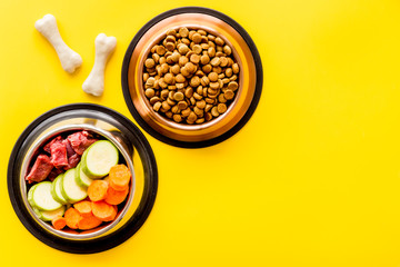 Ingredients of dry feed for dogs - meat, vegetables - near bones on yellow background top view copy space