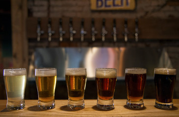 Bar sample drinks. Different kinds of craft beer in glasses with the beer taps in the background