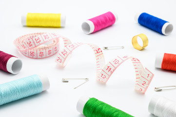 Sewing kit with measure tape, pins, colorful threads isolated on white background.