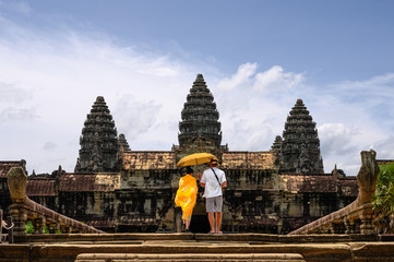 Two tourists Asian woman and European man protecting from the sunshine with an umbrella are entering the Angkor Wat temple in Siem Reap, Cambodia. UNESCO world heritage.