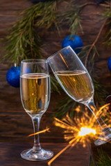 Glasses of champagne with bubbles on the background of Christmas decorations. Glasses touch during a festive toast and sparklers burn beautifully. Beautiful card.