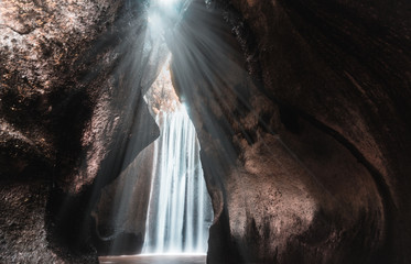 The rays of sun are shining through the mountain over the Tukad Cepung waterfall on Bali, Indonesia. Famous travel destination, hidden waterfall between the rocks.