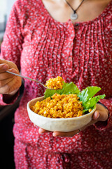 Bulgur cereal cooked. In bowl with vegetables. Vegan, vegetarian food. Woman holds in hands on legs a bowl with bulgur pilaf.