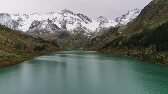 Drone fly above milky green water of alpine Multa lake surround with snowy range
