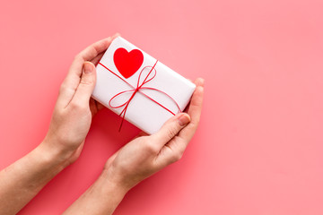 Give a gift on Valentine's Day. Women hand hold present box decorated with small heart on pink background top-down copy space