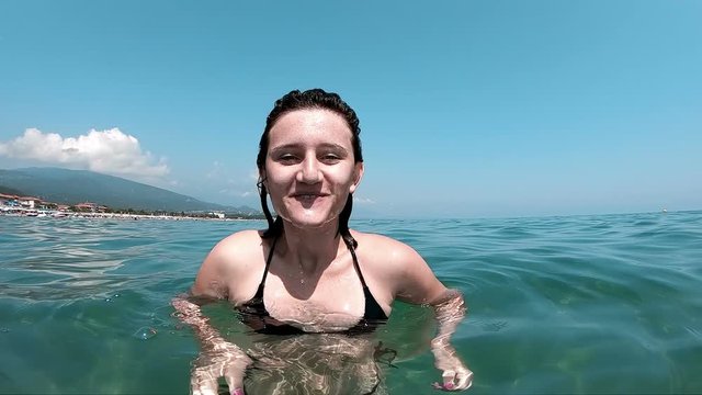 Happy silly girl spitting water in the camera in the sea