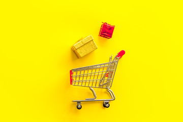 Gifts shopping. Present boxes and cart on yellow background top-down copy space