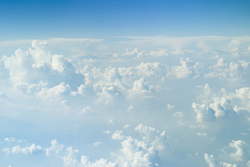 Large white cumulus clouds against the blue horizon, view from the airplane window.