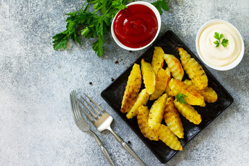 Fast food. Baked potatoes with spices, slices on slate or stone, served with mayonnaise and ketchup sauce. Top view on a flat background. Copy space.