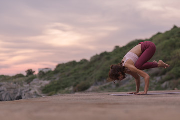 Young woman doing exercise yoga doing Crane (Crow) pose. Amazing yoga landscape in beautiful sky...