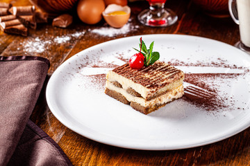 Italian food concept. Coffee dessert Tiramisu made with Savoyardi cookies and mascarpone cream, a knife and a fork of cocoa. Serving dishes in a restaurant. background image