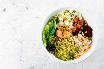 Top view of healthy pumpkin seasonal bowl. Salad with meat, cheese, bulgur and vegetables on marble background. Copy space