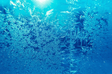 Fototapeta na wymiar Ice freezes on glass in the cold winter season. Beautiful blue patterns left by frost on the window create the atmosphere of the New Year or Christmas holiday or other event.