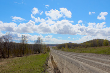 Fototapeta na wymiar Beautiful spring day after rain in the countryside. Blue sky in the clouds and a road stretching into the distance. Early spring. The first leaves on the trees, green grass erupts. Selective focus