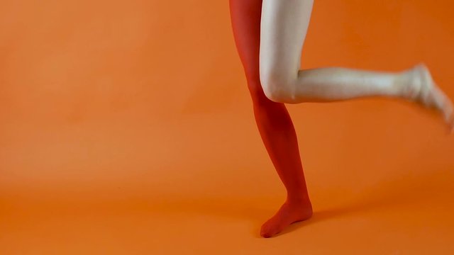 Female model is wearing red tights on the one leg, another leg is naked and without stockings on in studio over bright orange background