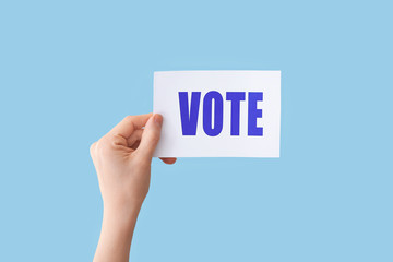 Hand holding paper with text VOTE on color background