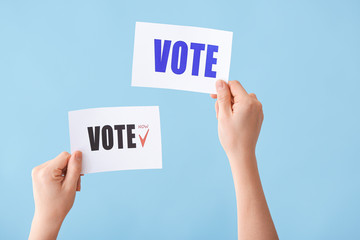 Hands holding papers with text VOTE on color background